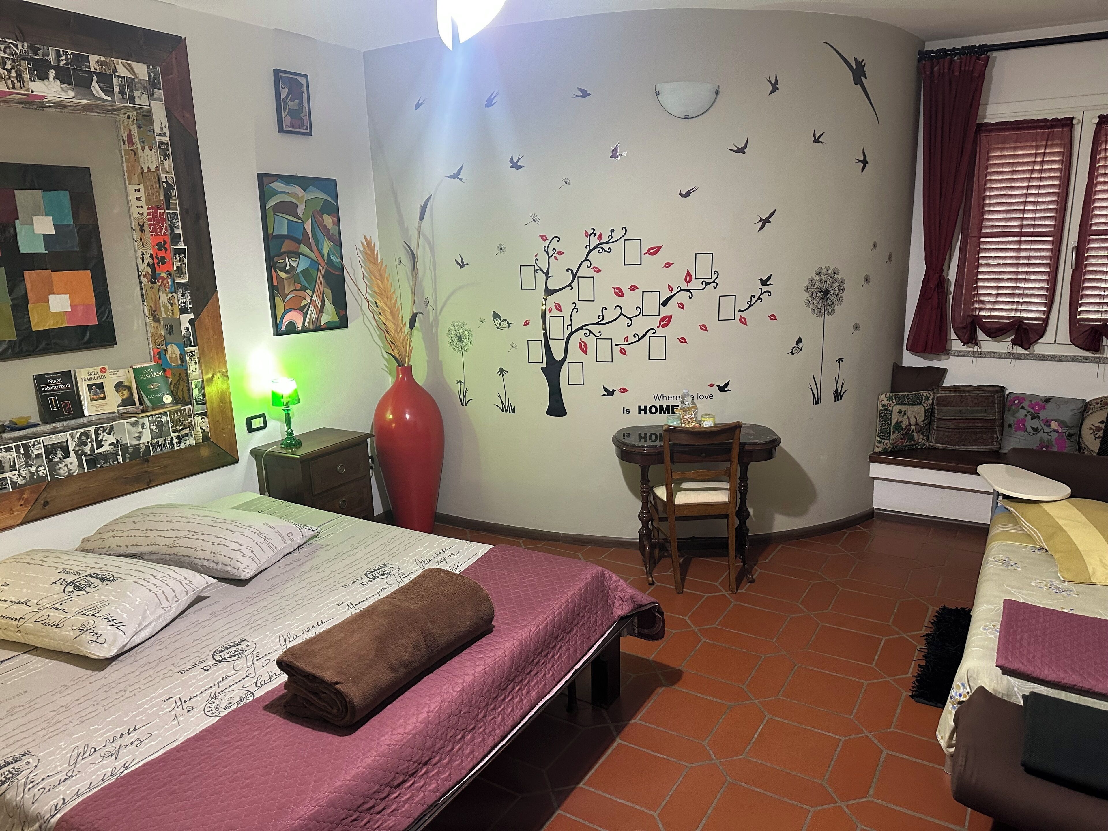 Ein gemütliches Schlafzimmer mit Bett, Schreibtisch und Stuhl. An der Wand ist eine Baum-Abbildung und ein Spiegel.