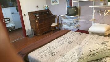 A bedroom with a bed, a wooden dresser, a television, and a small table with a chair.