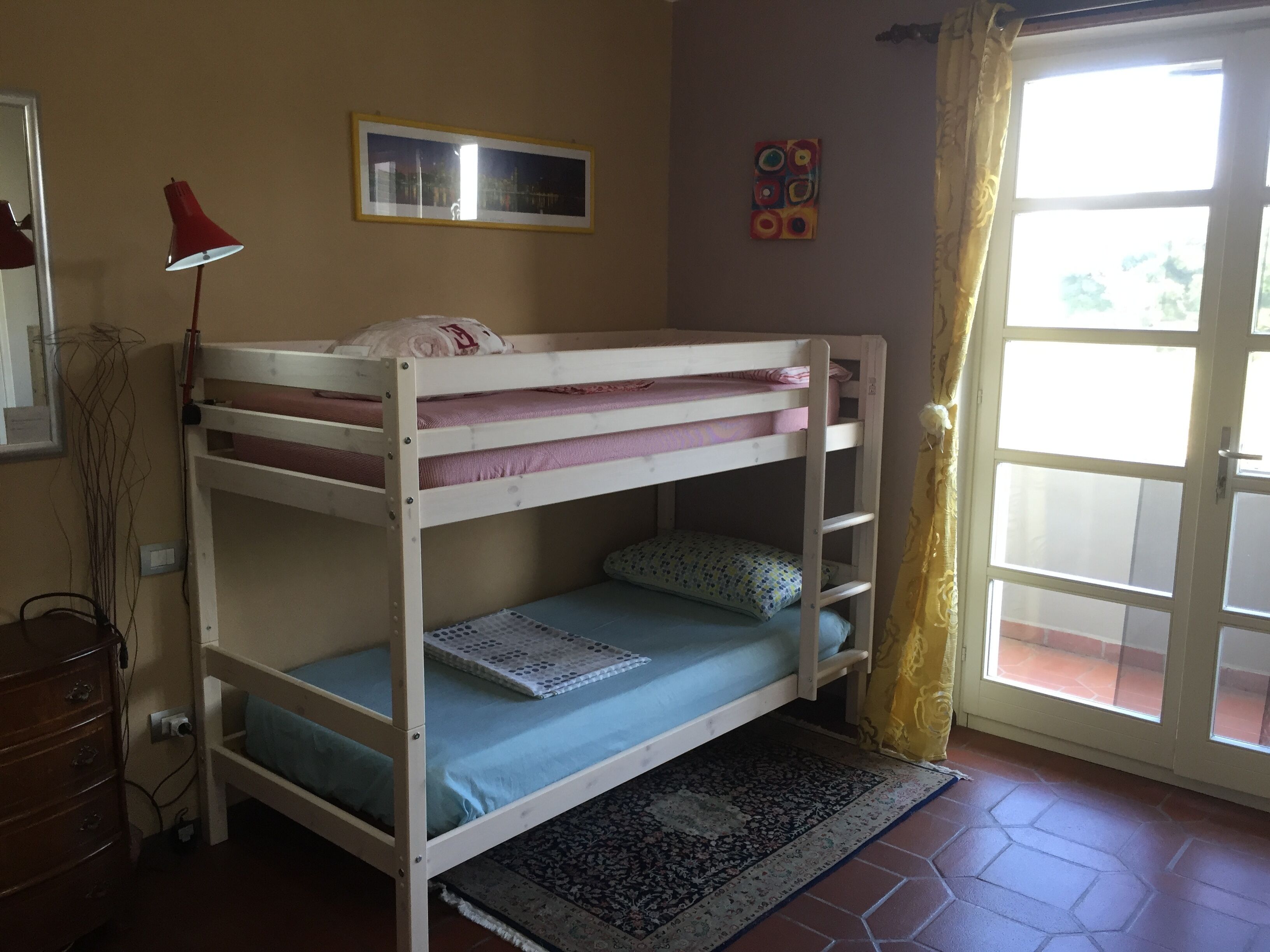 A bunk bed room with a window, a red lamp, and a small rug.