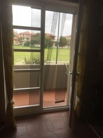 Una puerta corrediza de vidrio que da a un balcón con vistas a una zona residencial y un césped.