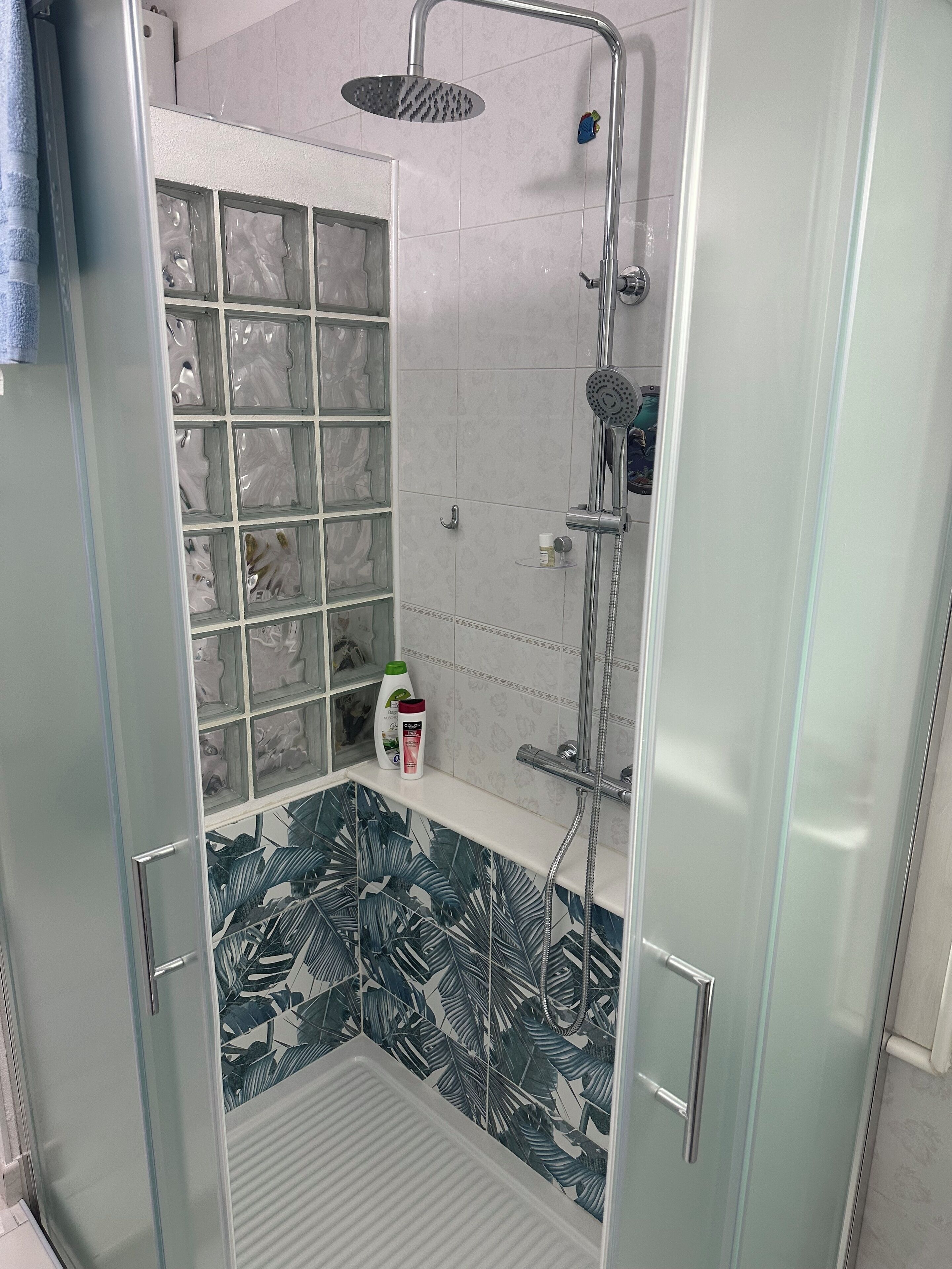 Ein modernes Badezimmer mit Duschkabine aus Glas, einer eingebauten Ablage mit Pflegeprodukten und einer dekorativen Fliesenrückwand.