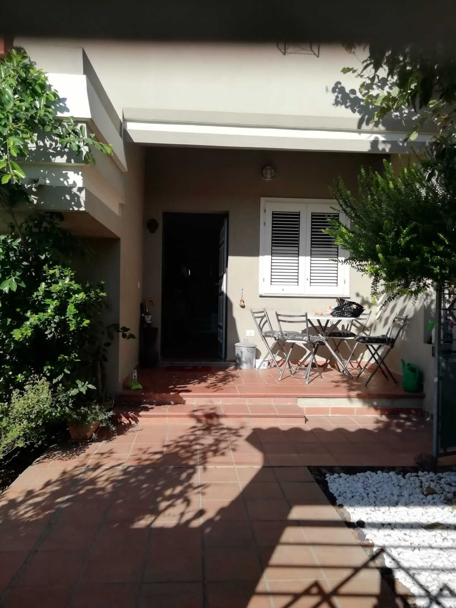 A house with a tiled patio, a door, a window with shutters, and a table with chairs.