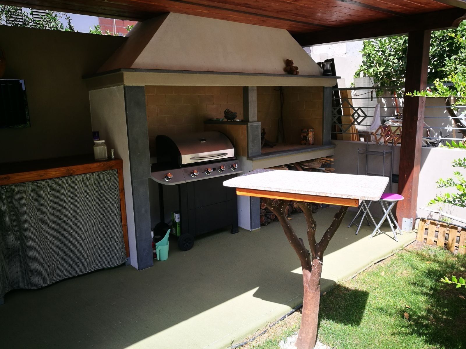 Una cocina exterior con una parrilla, una mesa y una silla.