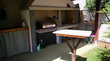 Una cocina exterior con una parrilla, una mesa y una silla.