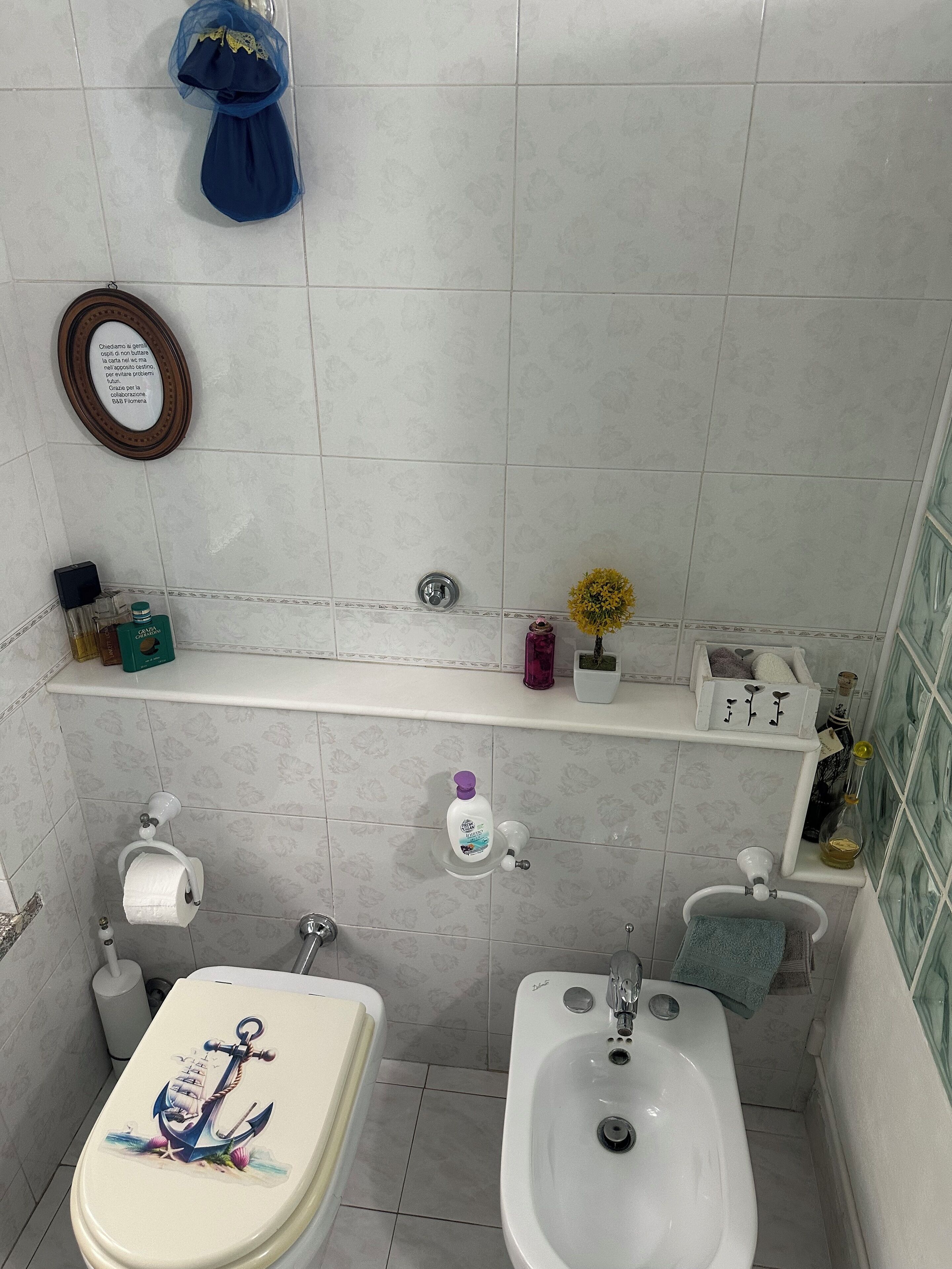 A bathroom with a toilet, bidet, and a shelf with toiletries.