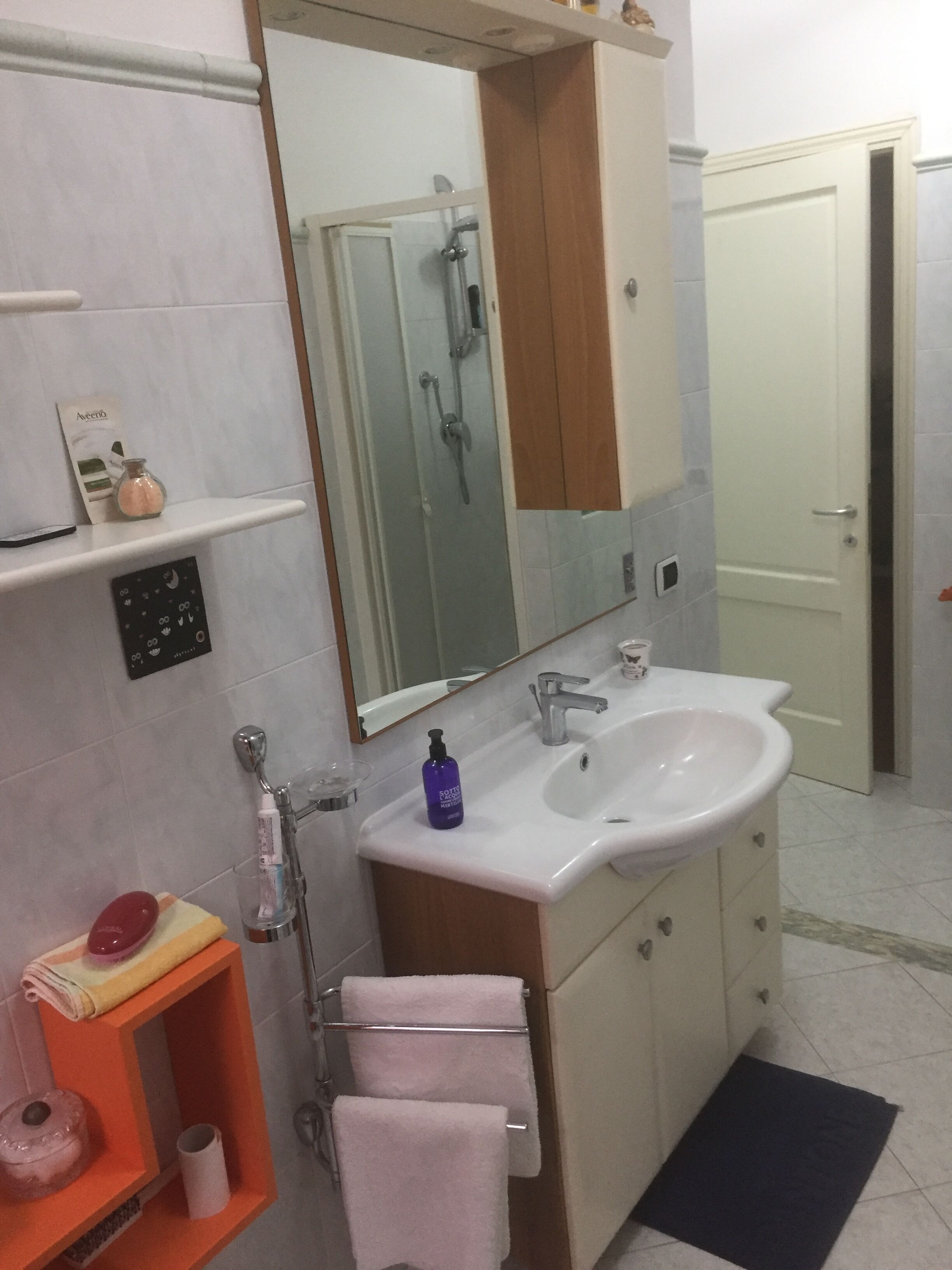 Un baño con un lavamanos blanco, un espejo, una ducha y un toallero.