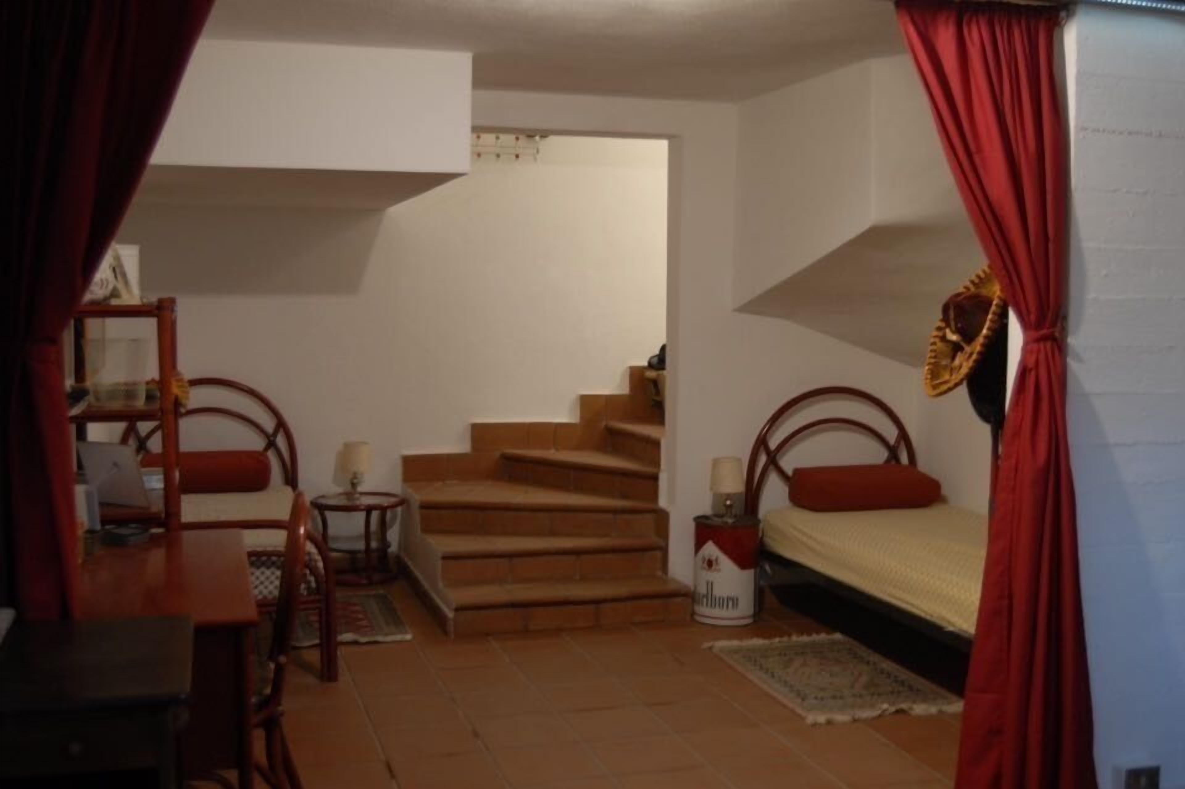 A bedroom with a bed, a desk, a chair, a lamp, and a staircase.