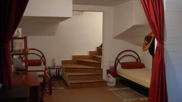 A bedroom with a bed, a desk, a chair, a lamp, and a staircase.