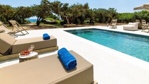 A poolside area with lounge chairs, a pool, and a view of the sea. - Beachfront Villa Akti (Gennadi area)