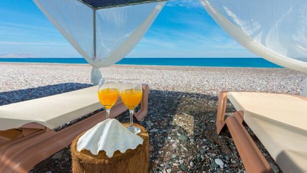 A beachside lounge with two lounge chairs, a table with two glasses of orange juice, and a wooden stump. - Beachfront Villa Akti (Gennadi area)