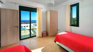 A bedroom with two beds, a wardrobe, and a sliding glass door leading to a balcony. - Beachfront Villa Akti (Gennadi area)