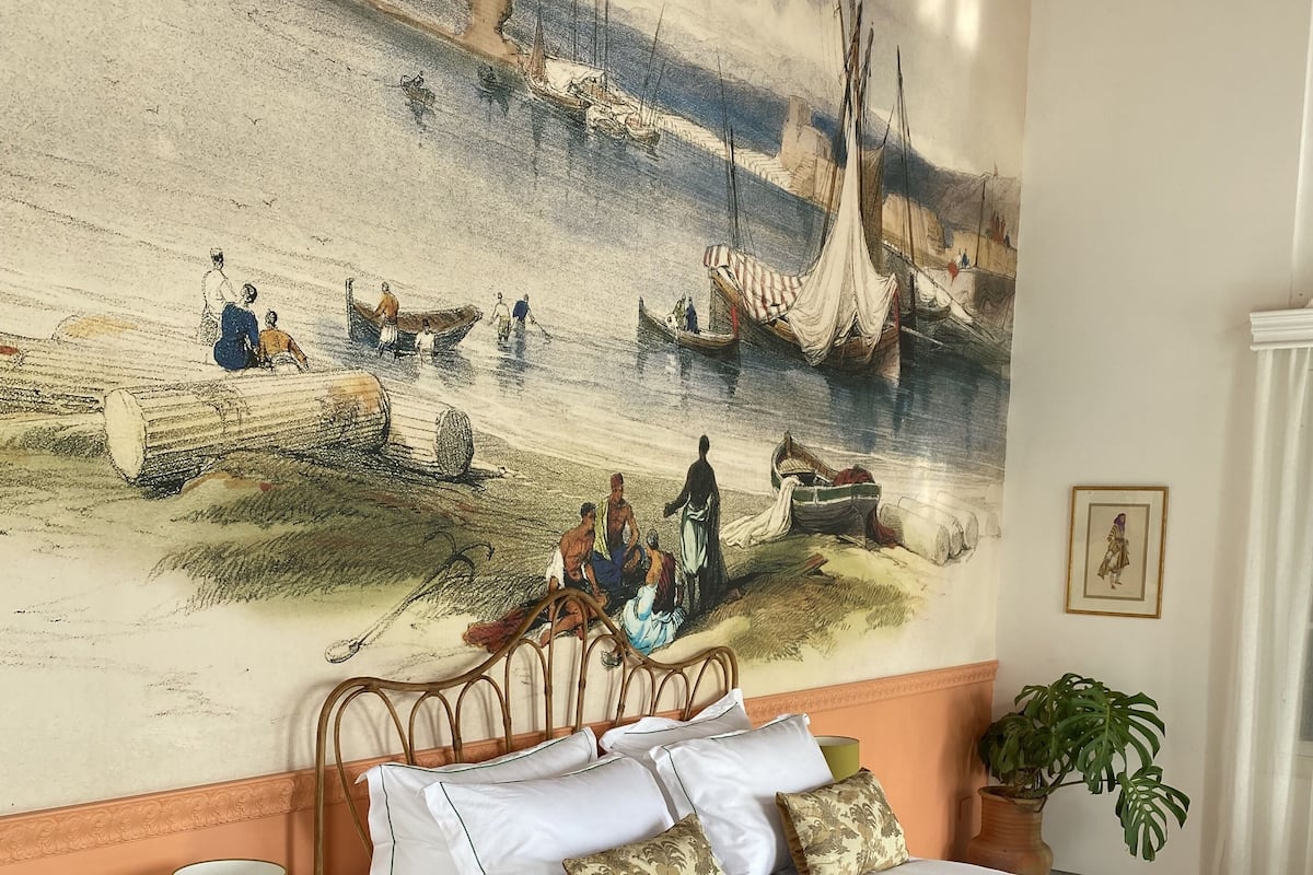 A bed with white linens, a brown throw blanket, and a green lamp beside it.