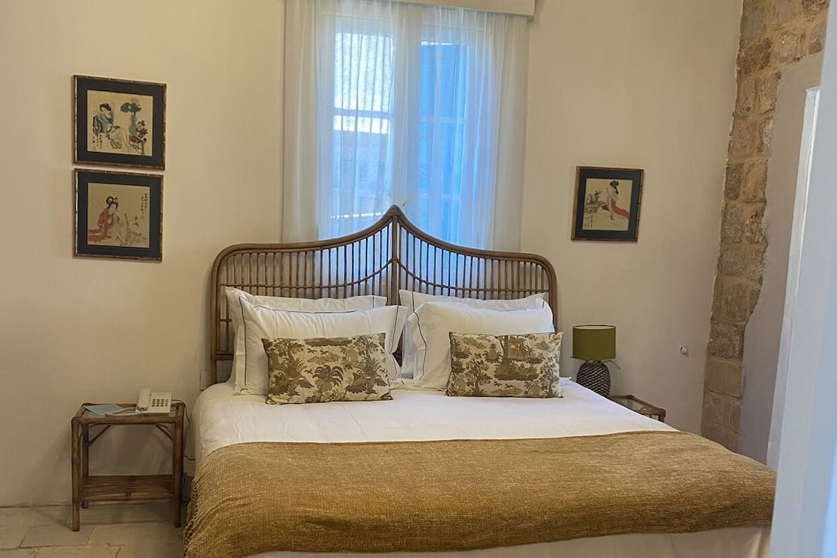 A bedroom with a wooden bed, white bedding, a small bedside table with a lamp, and two framed pictures on the wall.