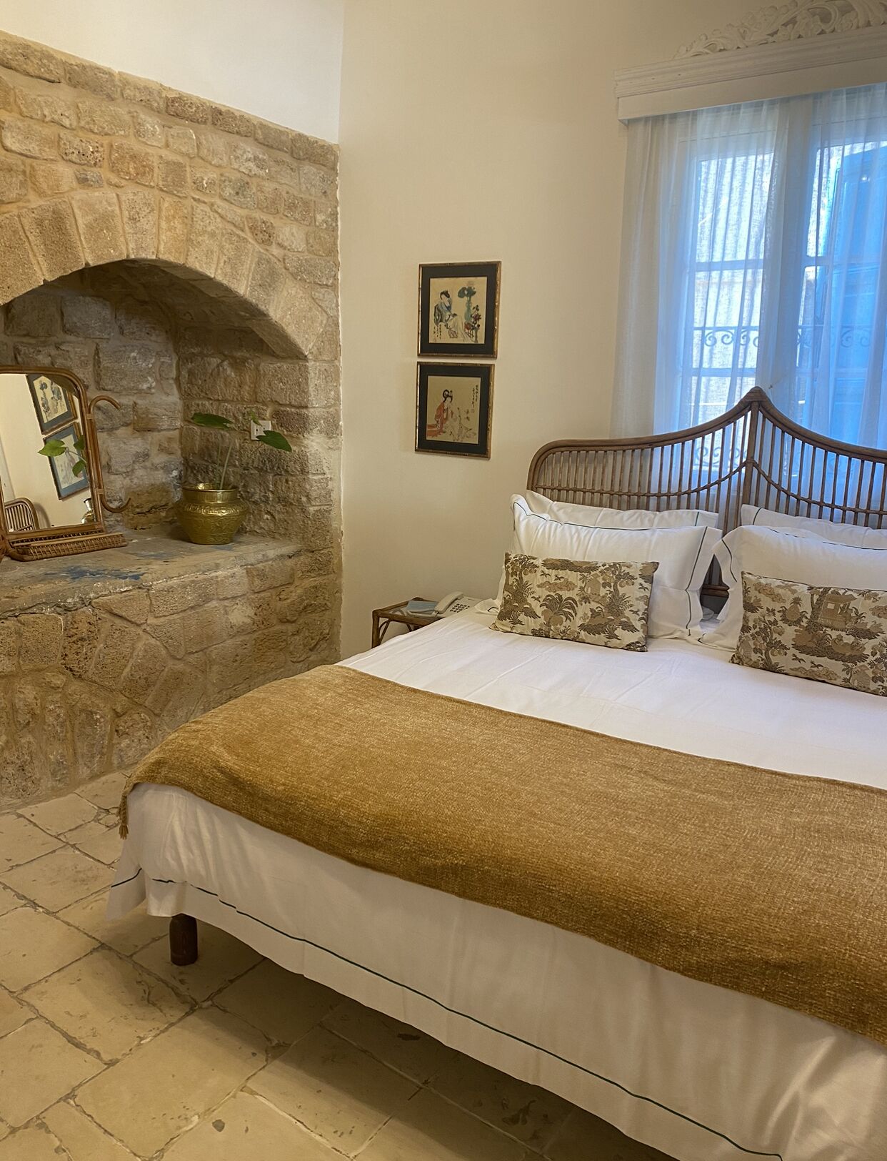 A bedroom with a stone fireplace, a bed with a gold throw, and two framed pictures on the wall.