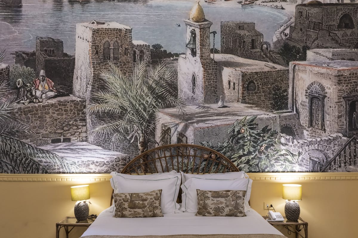 A bedroom with a bed, two bedside tables, and a view of a coastal town with buildings and a lighthouse.
