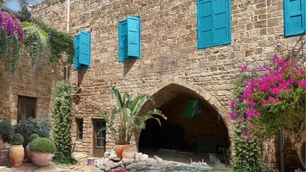 A stone building with blue shutters, a swimming pool, and a garden with potted plants and flowers. - Dar Alice (Tyre)