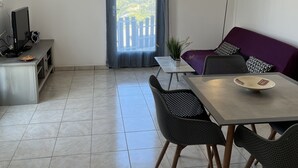 Een moderne woonkamer met een eethoek, een televisie en uitzicht op een stadslandschap door een raam.