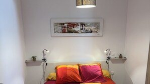Een slaapkamer met een bed voorzien van een kleurrijke quilt, twee nachtkastjes met lampen, een hanglamp en een lijst met een kunstwerk aan de muur.