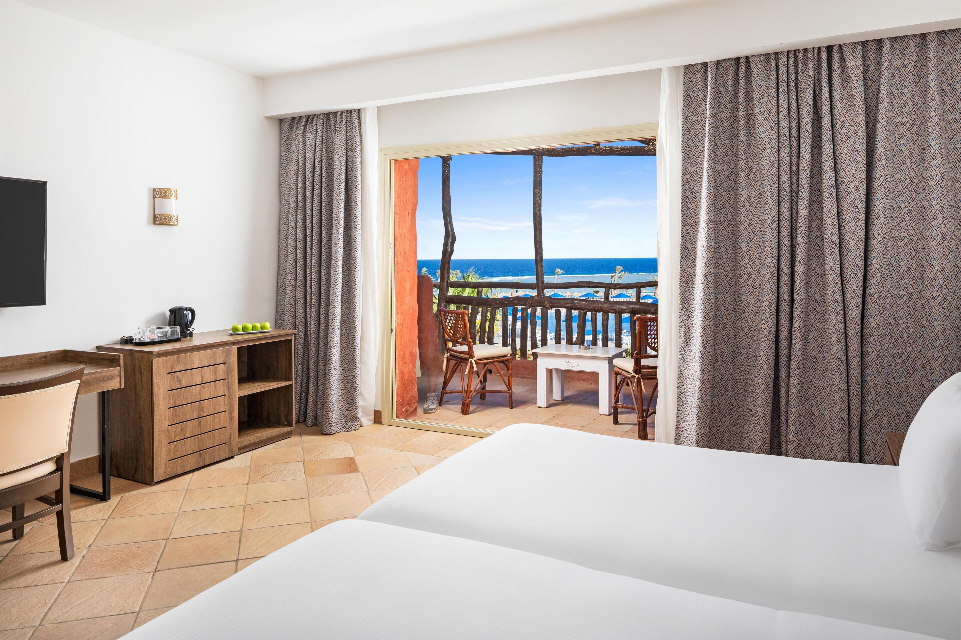 Camera d'albergo con un letto, una scrivania con una sedia, un tavolino con sedie e vista sull'oceano.
