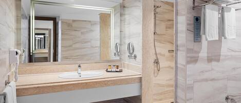 A modern bathroom with a marble vanity, a large mirror, a shower with a handheld showerhead, and a towel rack with folded towels.