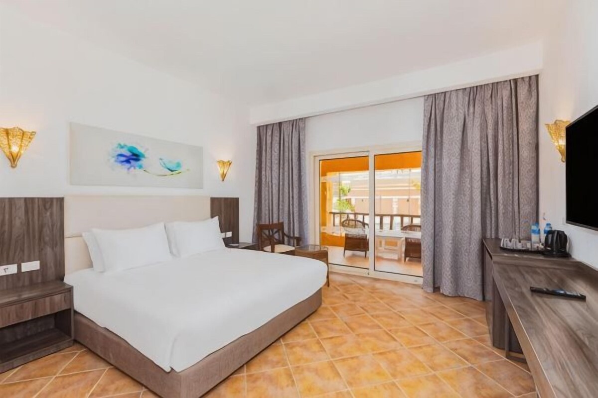 Een hotelkamer met een groot bed, een bureau, een televisie en een balkon met gordijnen.