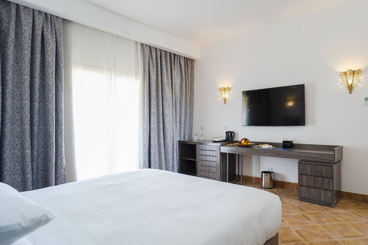 Een hotelkamer met een bed, een bureau met een flatscreen televisie en een kleine keukenhoek.