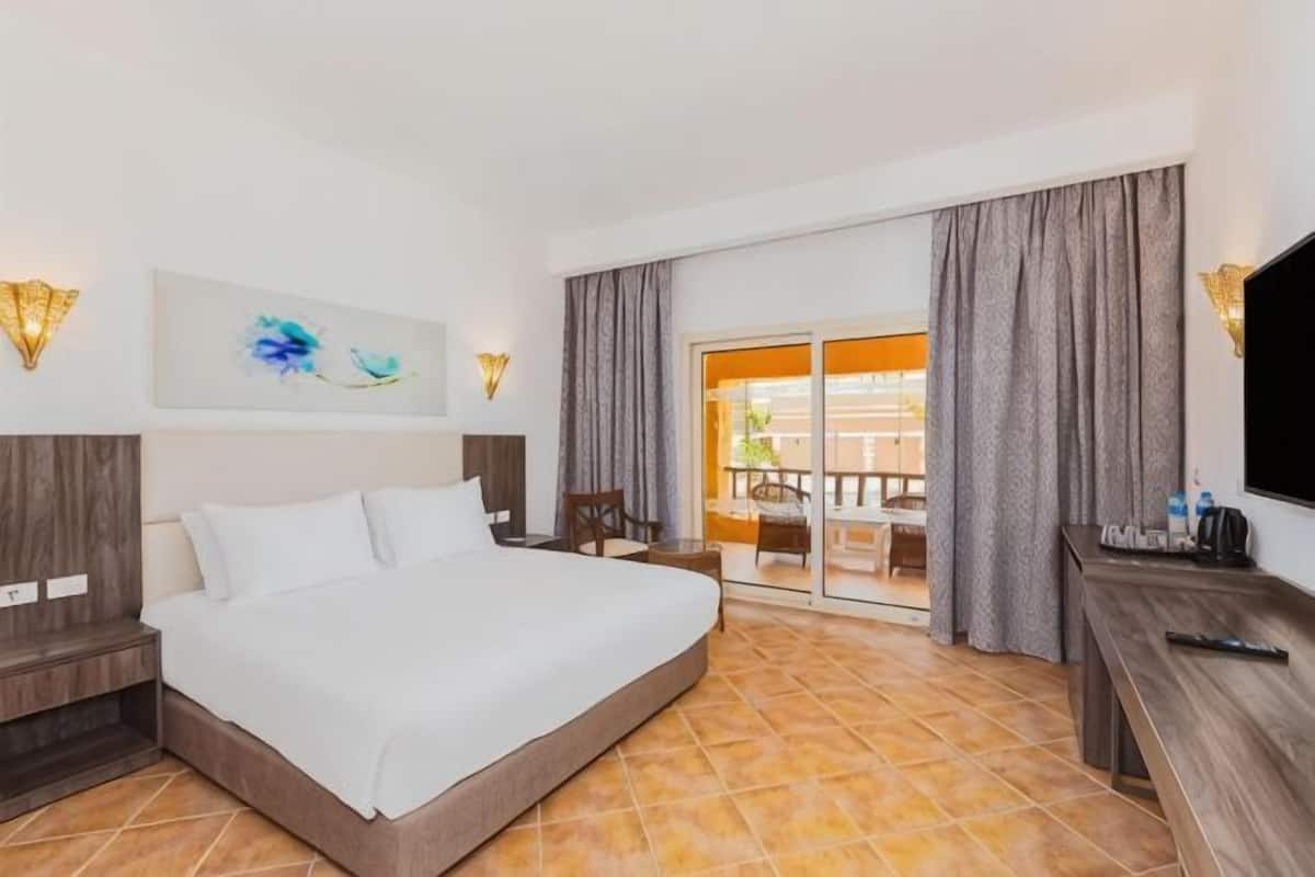 Een hotelkamer met een bed, een bureau, een televisie en een balkon met gordijnen.