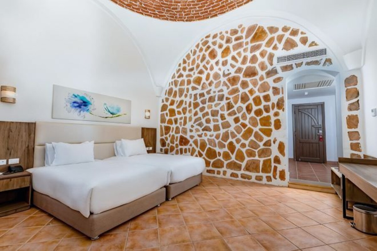 Une chambre à coucher comprenant un lit, une table de chevet, une œuvre d’art accrochée au mur, un mur en pierre et une porte donnant sur une autre pièce.