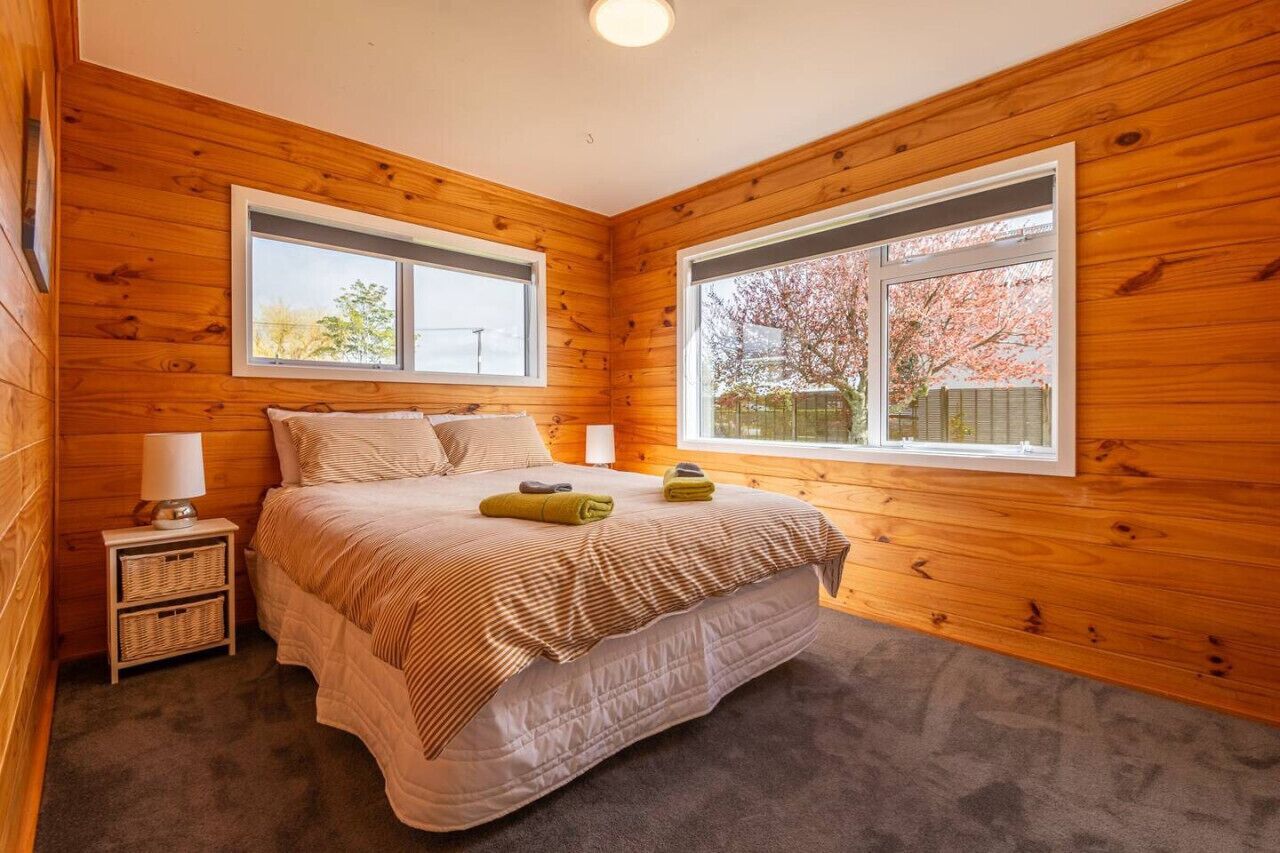 A wooden-paneled bedroom with a bed, two bedside tables, and large windows.