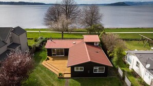 Una casa con techo rojo, terraza de madera y vista al lago.