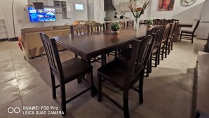 A spacious dining area with a long table and multiple chairs, a television mounted on the wall, and a kitchen in the background. - 150 sq. m. apartment in villa with private pool and Jacuzzi (Fabrica di Roma)