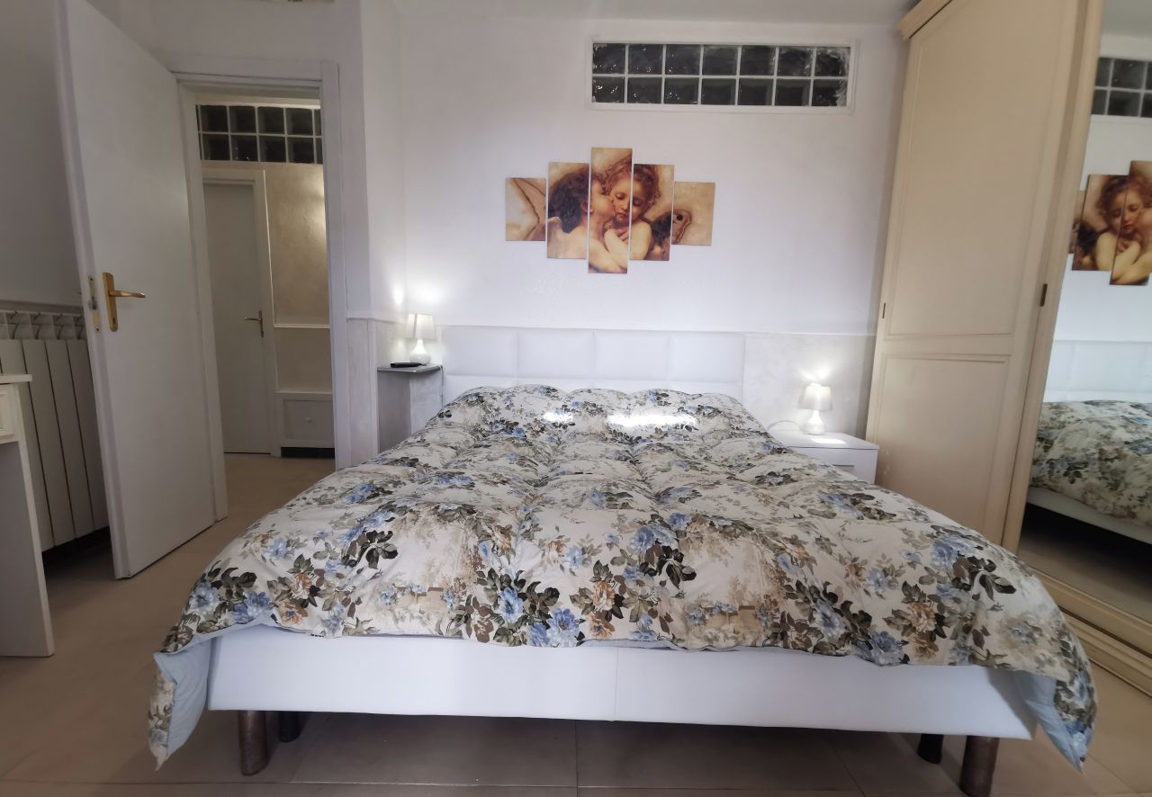 Um quarto com colcha florida, cabeceira branca, mesa de cabeceira com abajur e espelho na parede.