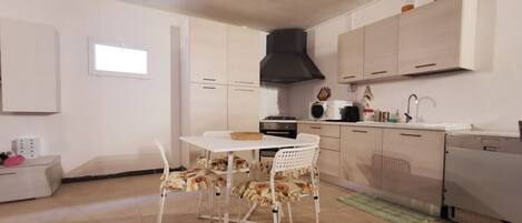 A compact kitchen with white cabinets, a black range hood, a microwave, and a sink. There is a small window and a green rug on the floor.