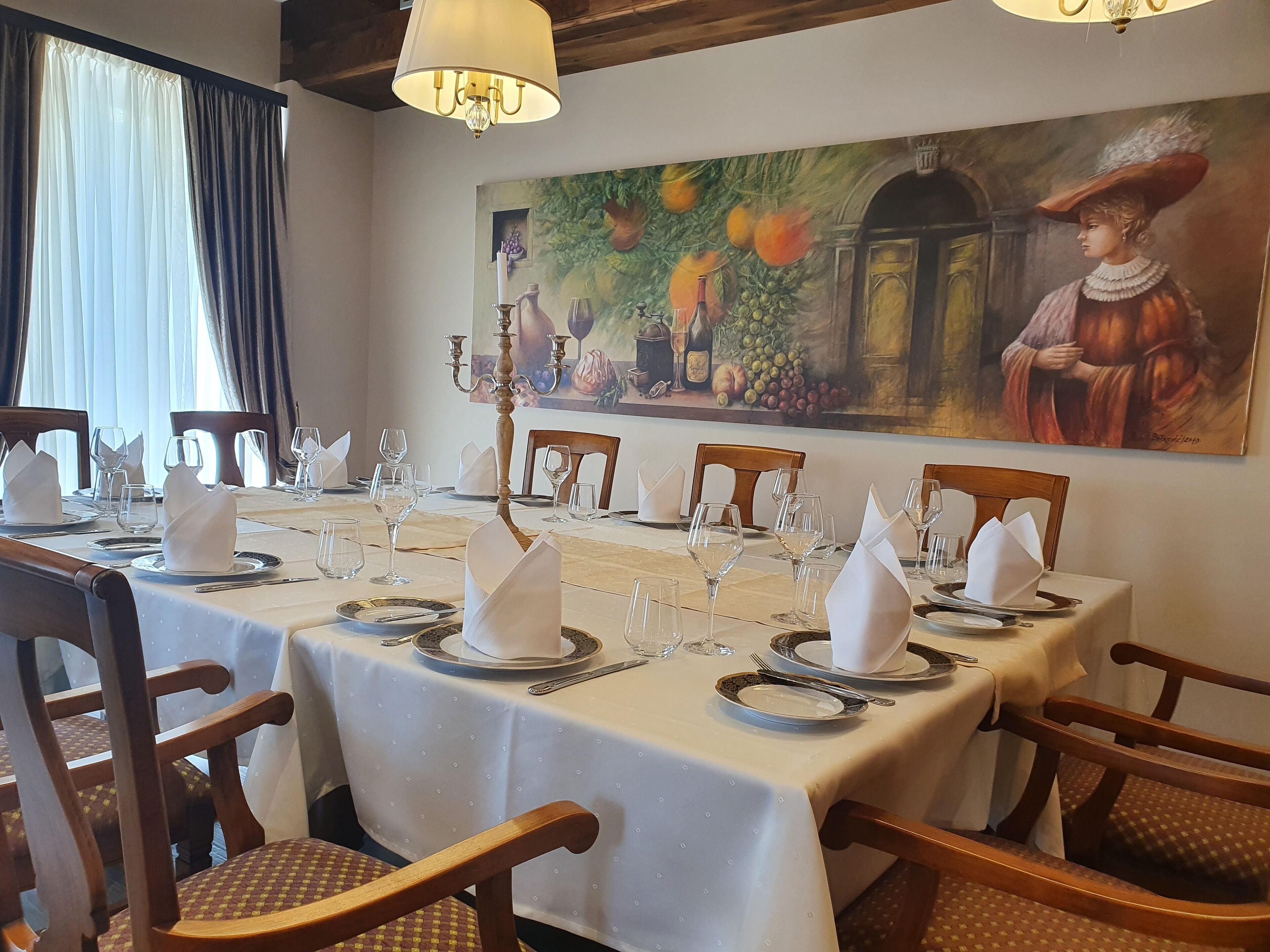 A dining area with a long table set for a meal, wooden chairs, and a painting on the wall.