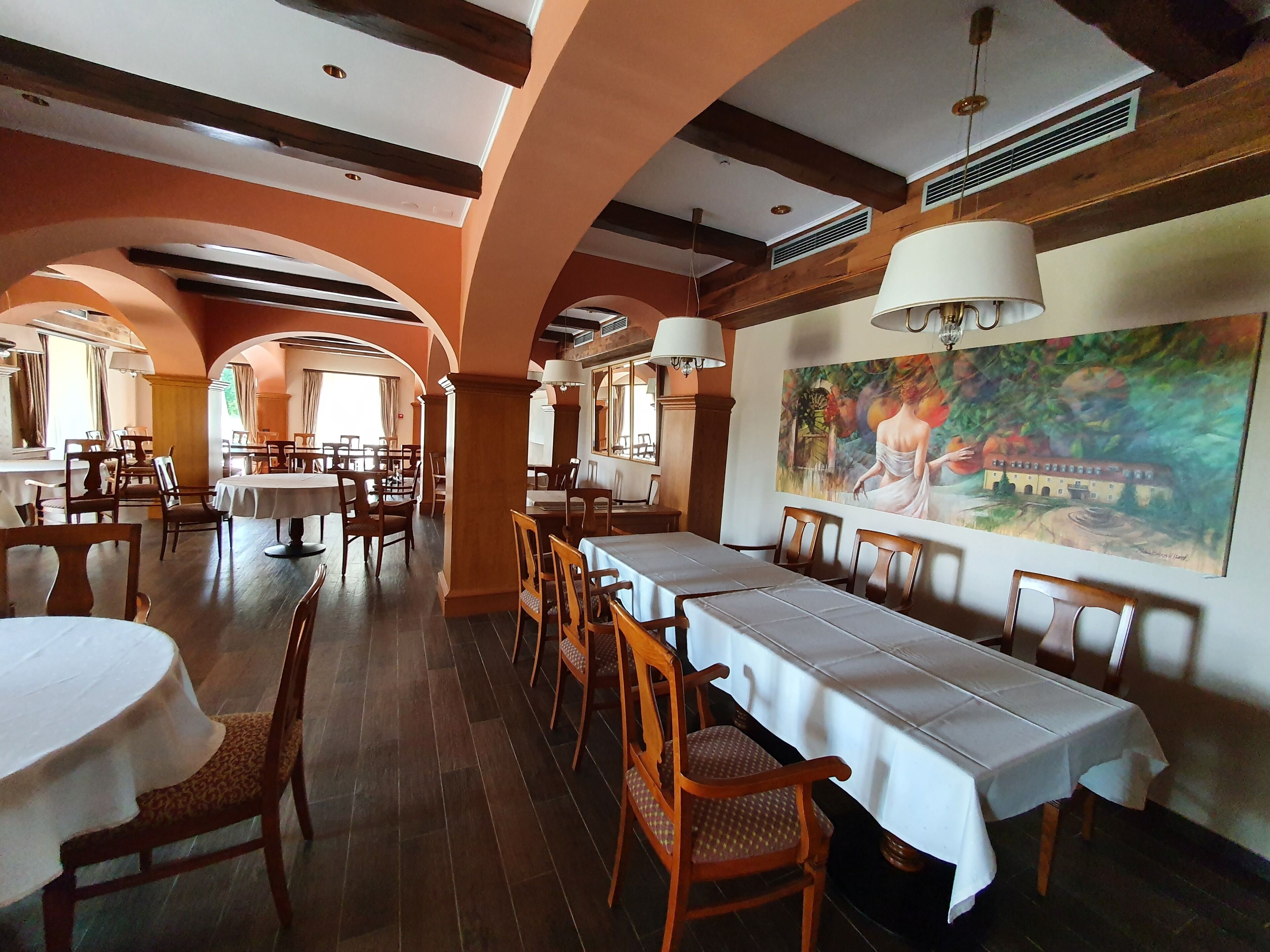 Un ristorante con tavoli comuni lunghi, sedie di legno e un grande murale sulla parete.