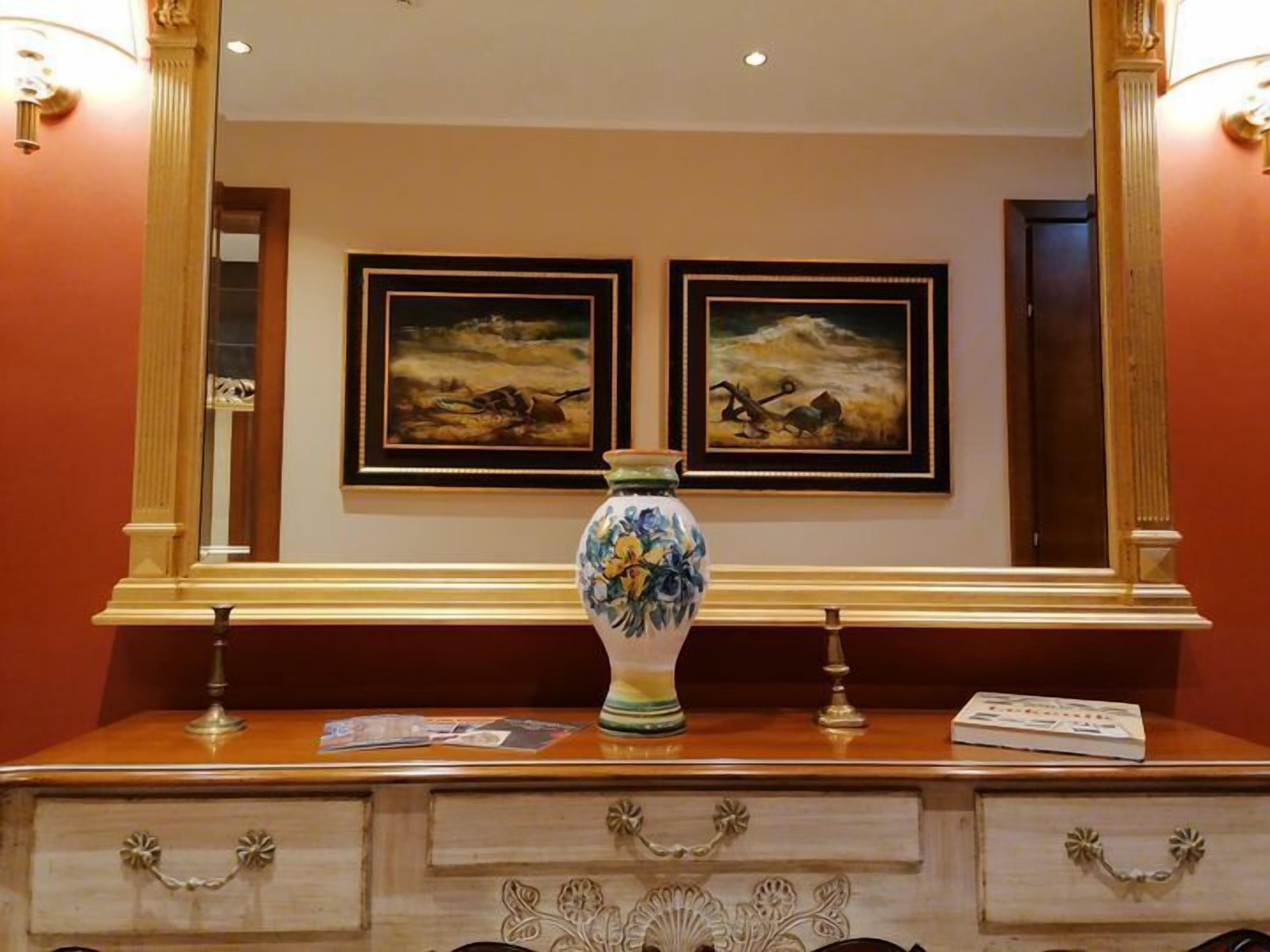 A wooden dresser with a vase and framed paintings on the wall behind it.