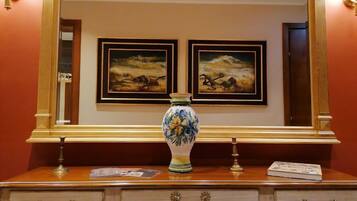 A wooden dresser with a vase and framed paintings on the wall behind it.