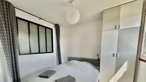 A bedroom with a bed, a wardrobe, and a window with curtains. - Capucine, Duplex à 5 min de la mer (Courseulles-sur-Mer)