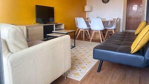 A modern living room with a sofa, a TV, a dining table with chairs, and a patterned rug. - Capucine, Duplex à 5 min de la mer (Courseulles-sur-Mer)