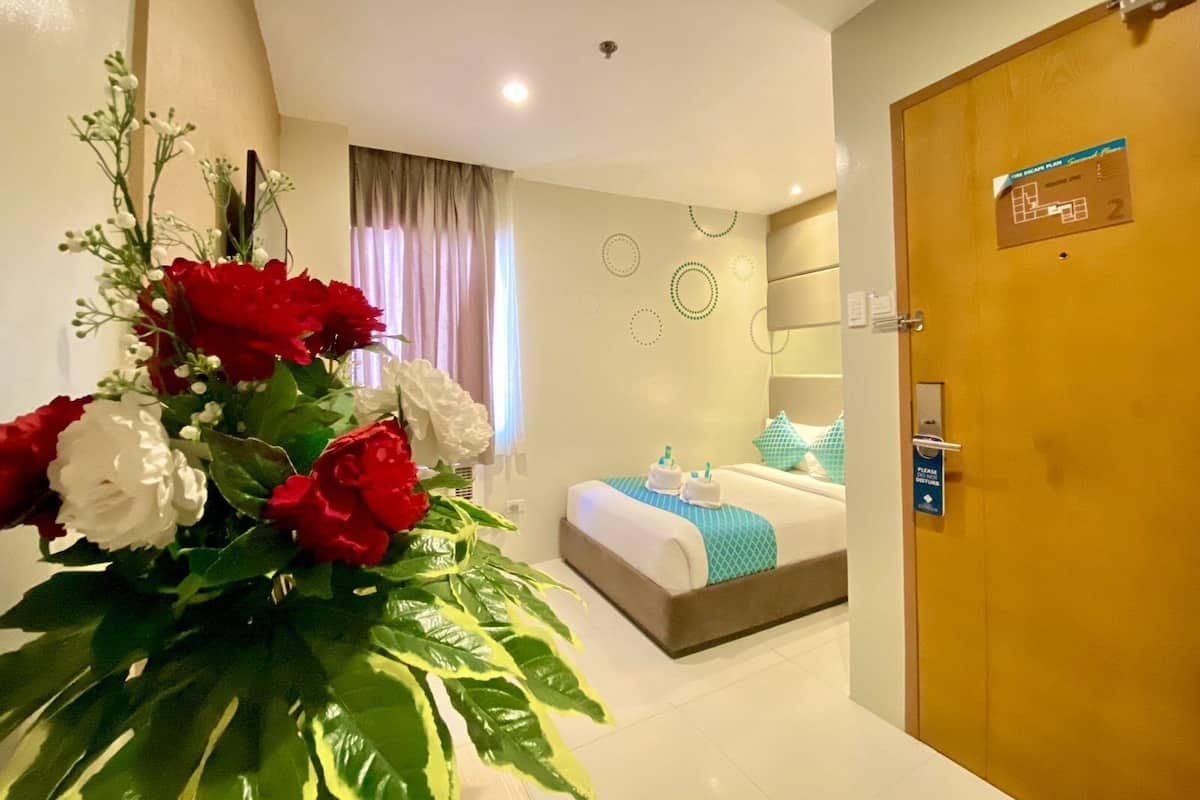 Ein Hotelzimmer mit Bett, Nachttisch, Blumen in einer Vase und einer Tür mit einem Schild.