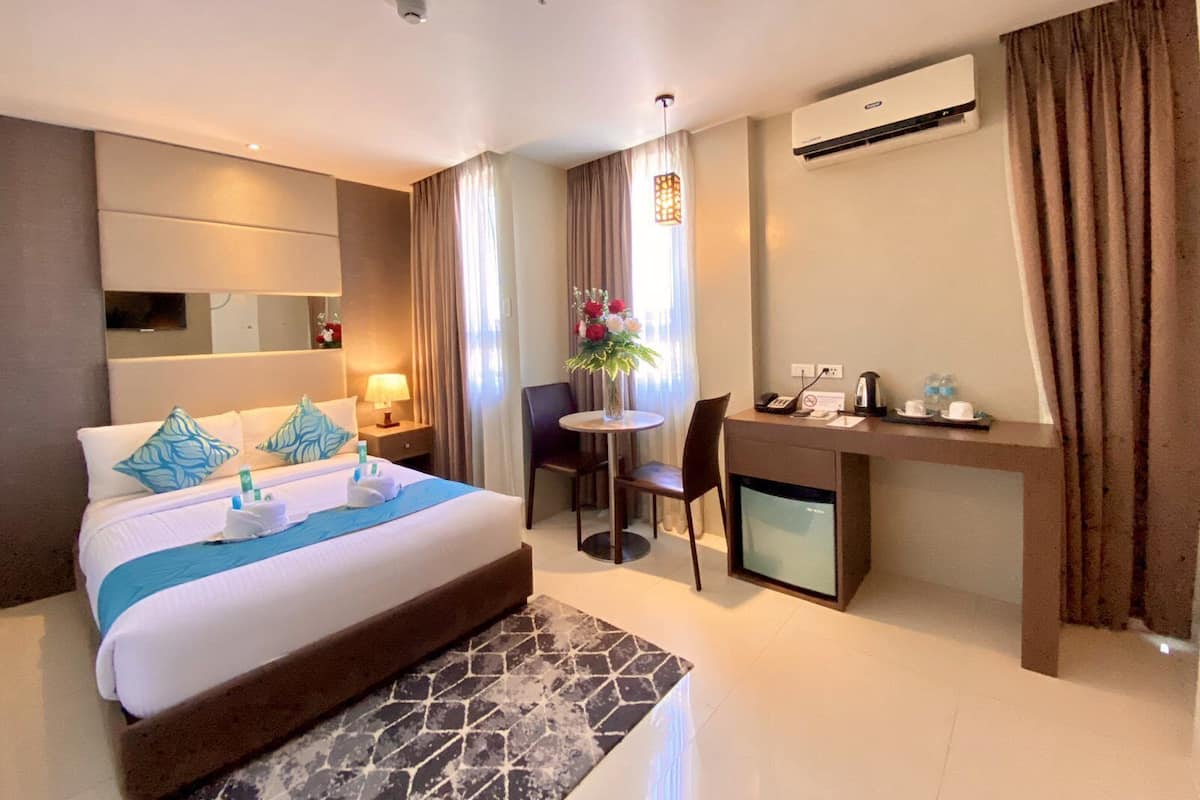 Ein Hotelzimmer mit Bett, Nachttisch, Lampe, Schreibtisch, Stuhl und kleinem Fernseher.