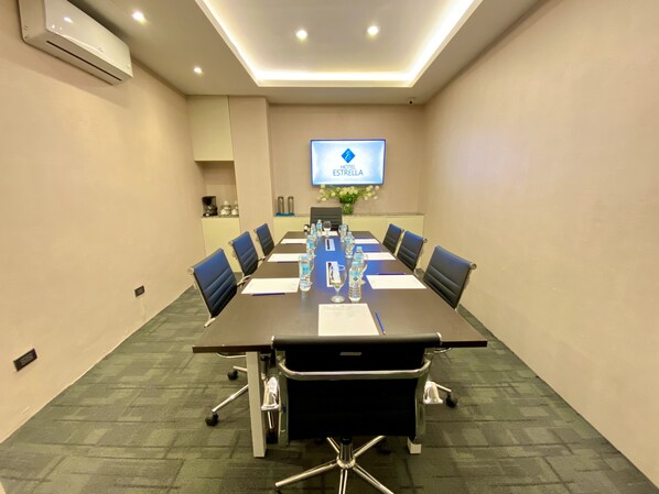 Un salón de conferencias con una larga mesa, sillas y una pantalla que muestra 