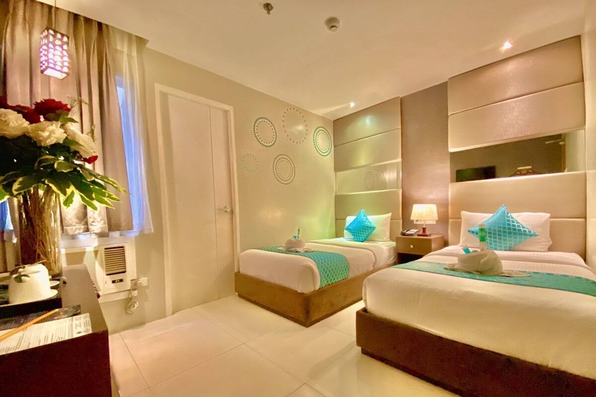 Ein Hotelzimmer mit zwei Betten, einem Schreibtisch und einem großen Fenster mit Vorhängen.