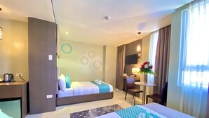 A hotel room with two beds, a desk, a chair, a small table with a lamp, and a TV. - Hotel Estrella (Tacloban)