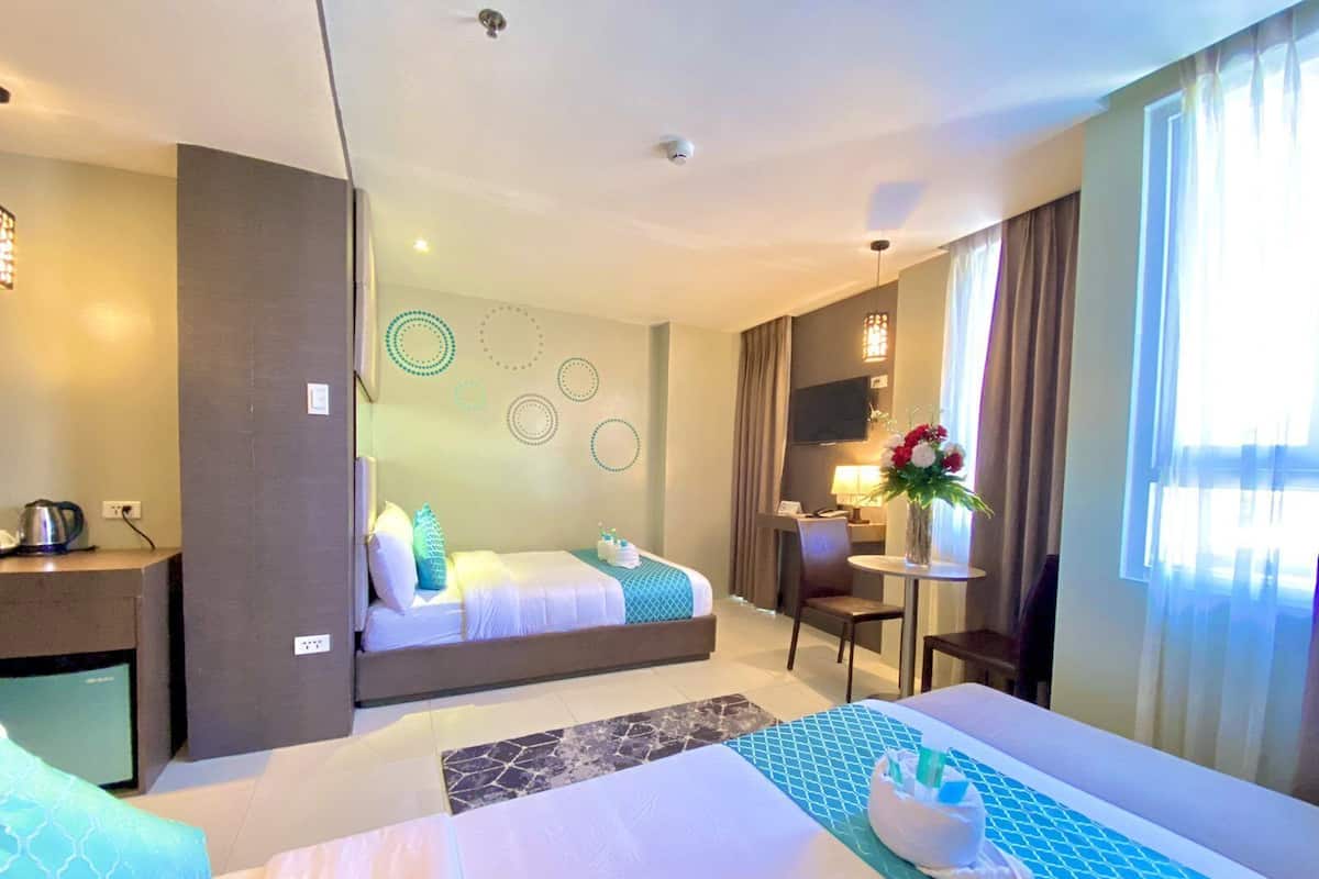 Ein Hotelzimmer mit zwei Betten, einem Schreibtisch, einem Stuhl, einem kleinen Tisch mit Lampe sowie einem Fernseher.