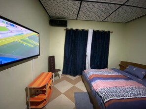 Ein Schlafzimmer mit Bett, einem an der Wand befestigten Fernseher, einem Sessel und einem kleinen Tisch.