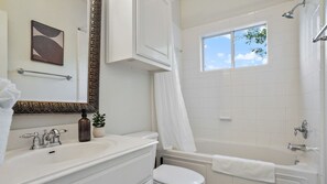 Une salle de bain moderne avec un lavabo blanc, un meuble-vasque, des toilettes et une baignoire. Une fenêtre laisse entrer la lumière naturelle et un porte-serviettes est placé au-dessus du lavabo.