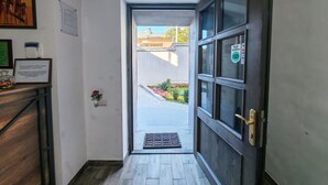 A hallway leading to a door with a glass panel, a framed certificate on a wooden desk, and a small potted plant. - Blur Inn Gallery Hotel (Yerevan)