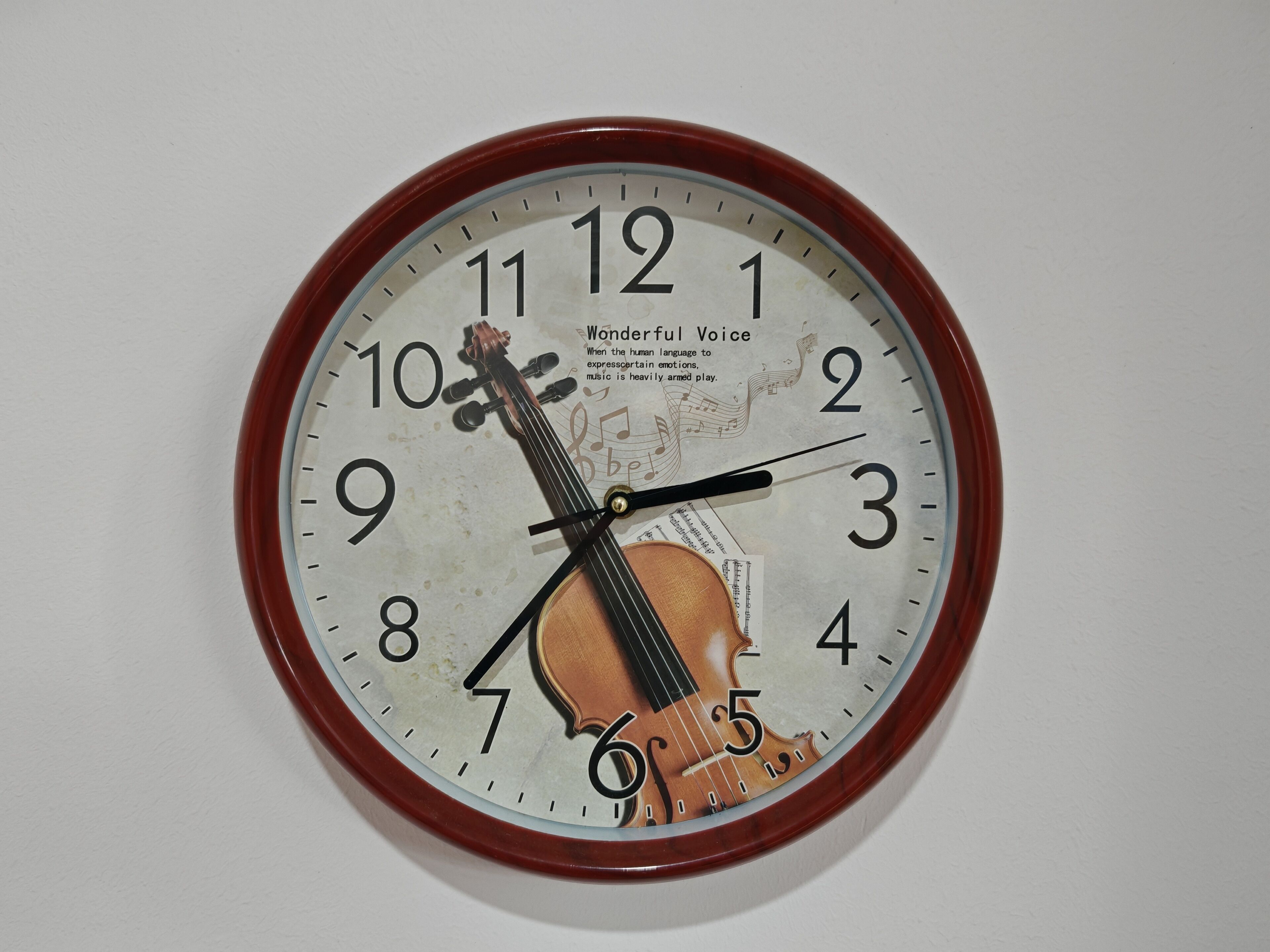 A wall clock with a musical theme, featuring a violin and sheet music.