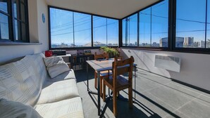 A balcony with a sofa, a table, and chairs, overlooking a cityscape through large windows. - Blur Inn Gallery Hotel (Yerevan)